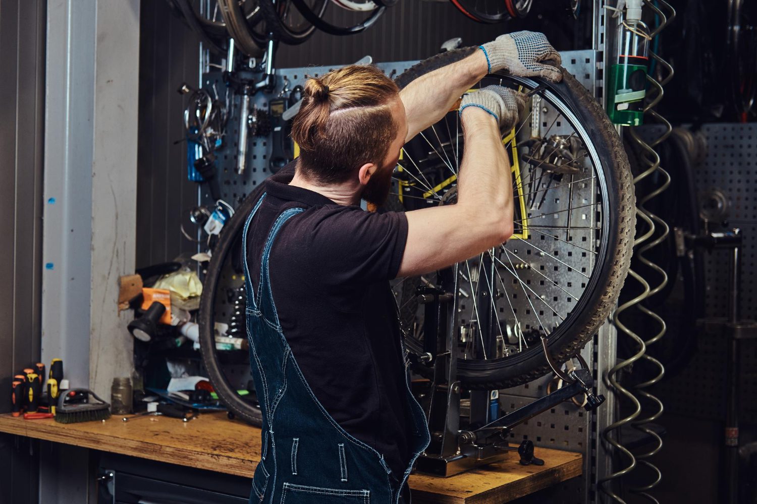 handsome-redhead-male-jeans-coverall-working-with-bicycle-wheel-repair-shop-worker-removes-bicycle-tire-workshop handsome redhead male jeans coverall working with bicycle wheel repair shop worker removes bicycle tire workshop